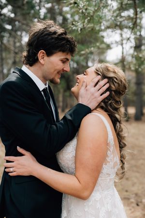 A romantic wedding couple embraces in a wooded setting while sharing a joyful moment together.