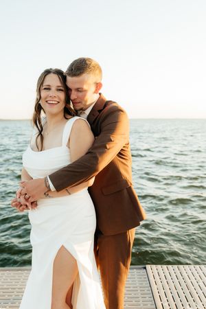 Couple in wedding attire sharing intimate moments on a waterfront dock at sunset.