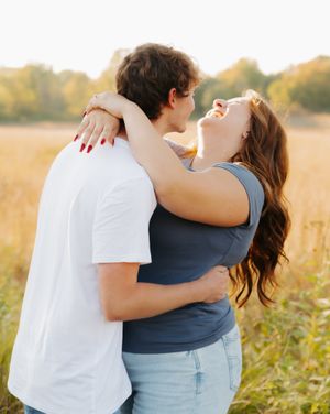 Couple embracing and laughing together in a sunlit meadow.