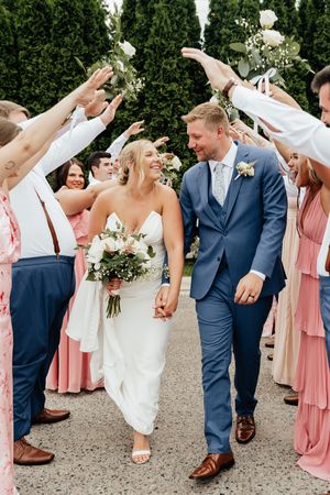 Wedding guests shower rose petals on a couple walking through an outdoor garden pathway.