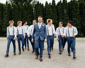 Wedding party in navy suits and suspenders walking together showing off colorful socks in a playful group photo.