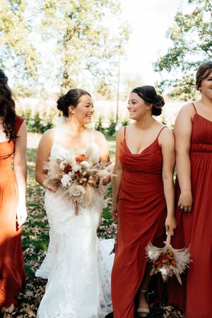 Wedding party in burgundy bridesmaid dresses and white bridal gown sharing joyful laughter outdoors.