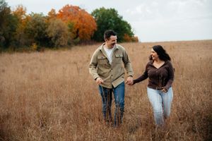 A couple walks through a golden autumn field during sunset holding hands.