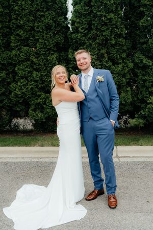 A couple shares joyful moments in formal wedding attire against a hedge backdrop.