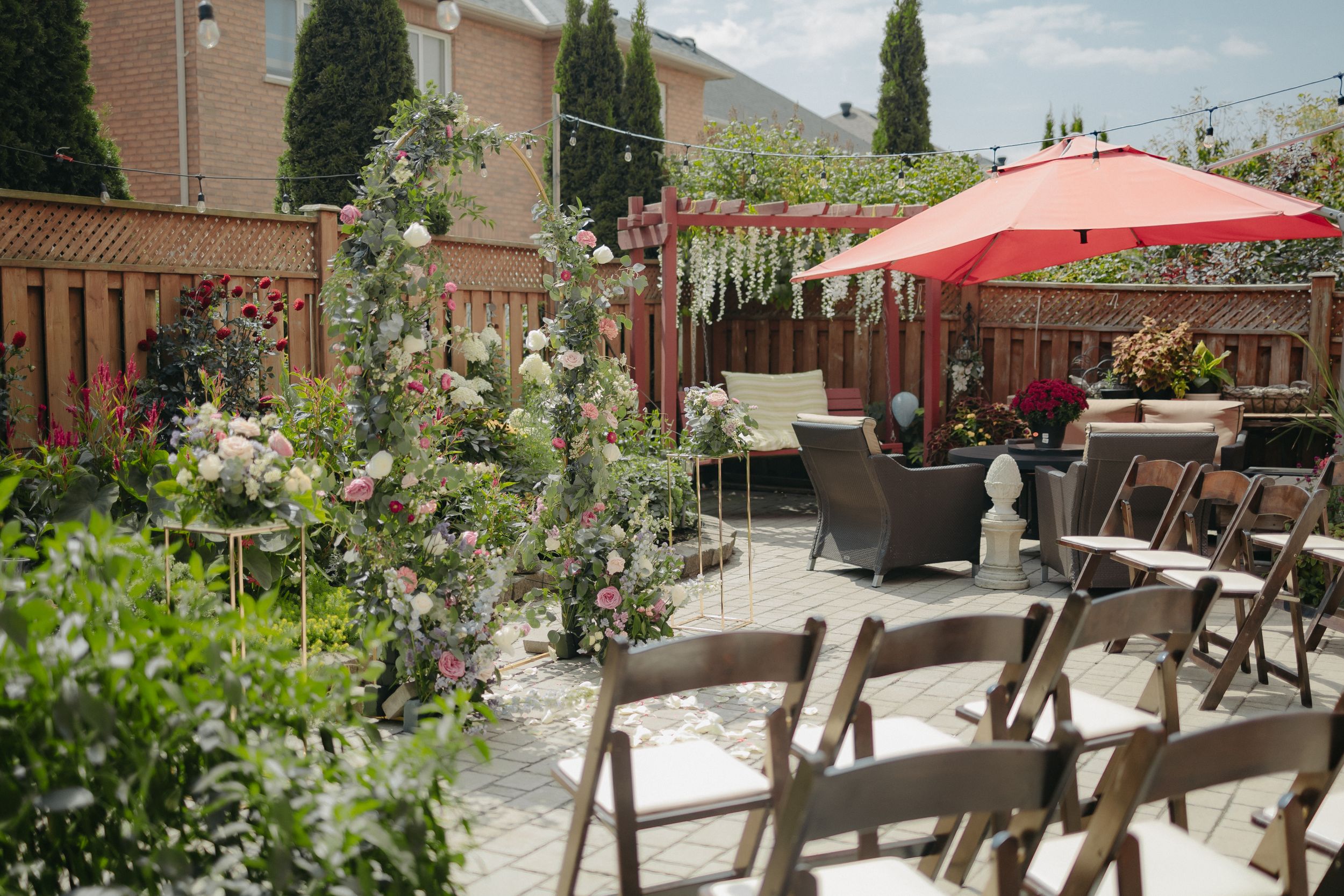 An outdoor wedding venue setup with folding chairs and garden decor under a red umbrella.