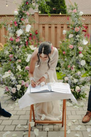 Someone signing wedding documents at a wooden table beneath a floral arch.