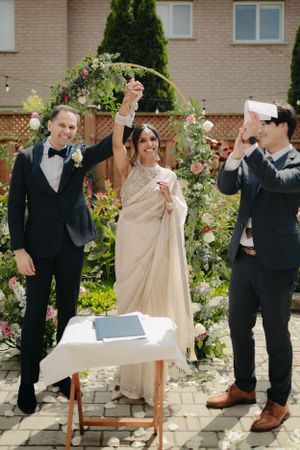 A celebratory moment after signing wedding documents under a floral arch in a garden setting.