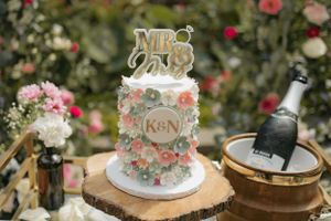 A delicate white wedding cake decorated with pink flowers and a 'Mr & Mrs' topper on a wooden slice.