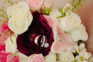 Wedding rings nestled inside a deep burgundy rose surrounded by pink and white flowers.
