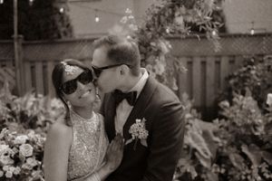 A black and white romantic portrait captured in a garden setting with a wooden fence backdrop.