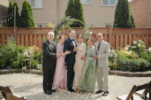 A group photo under a floral arch in a backyard garden with wooden fence and string lights.
