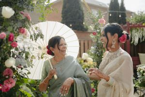 Two people share a laugh while holding white parasols in a flower garden.