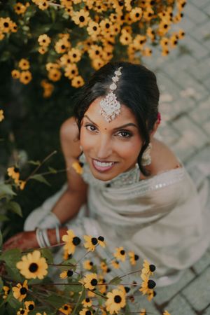 A bride in traditional Indian jewelry poses with sunflowers in the background.