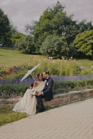 A couple shares an intimate moment on a garden wall surrounded by flowers.