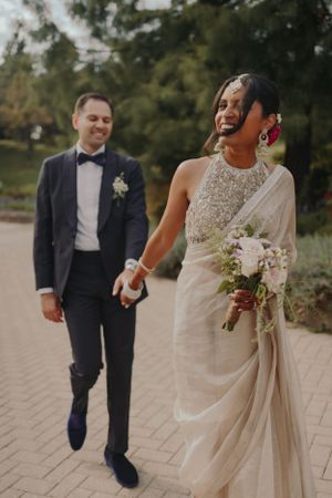 Newlyweds share a joyful moment walking together on a brick path as the bride holds a white bouquet.