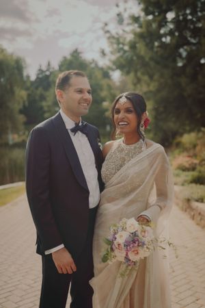 Wedding couple in formal attire pose for a portrait in a garden setting with natural greenery.