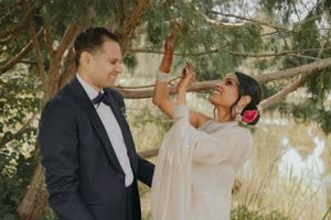 Wedding couple shares a playful moment outdoors under trees near a pond.
