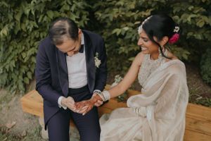 Intimate moment between newlyweds sitting together on wooden bench in garden setting.