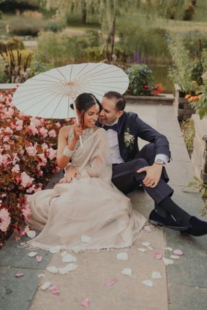 Romantic wedding photo with white parasol and scattered rose petals in garden setting.