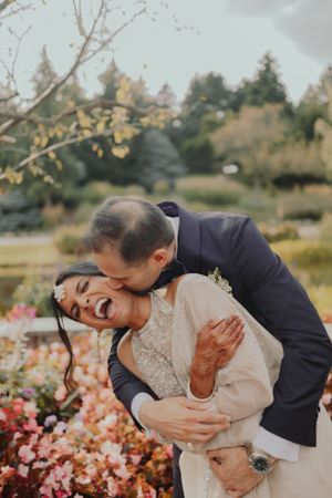 Candid moment of joy between newlyweds surrounded by pink flowers in garden setting.