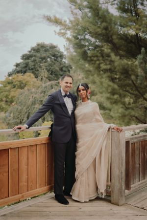 Newlyweds pose together on a wooden bridge surrounded by autumn trees.