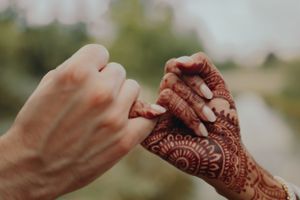 Close-up of hands with intricate henna design touching during a wedding celebration.