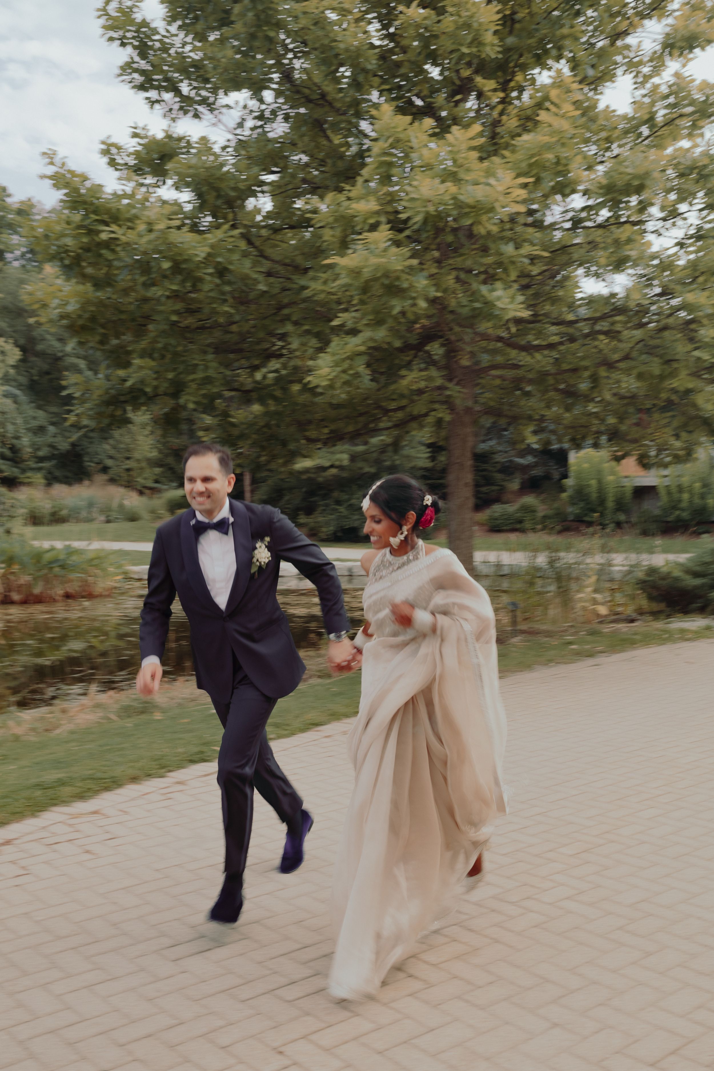 Playful couple running together on a paved path surrounded by autumn trees.