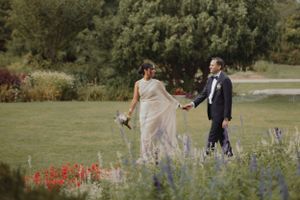 Couple standing in a garden with vibrant red flowers and purple wildflowers.