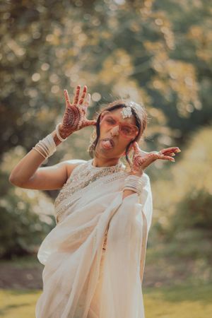 A playful moment captured of someone in white attire showing decorated henna hands outdoors.