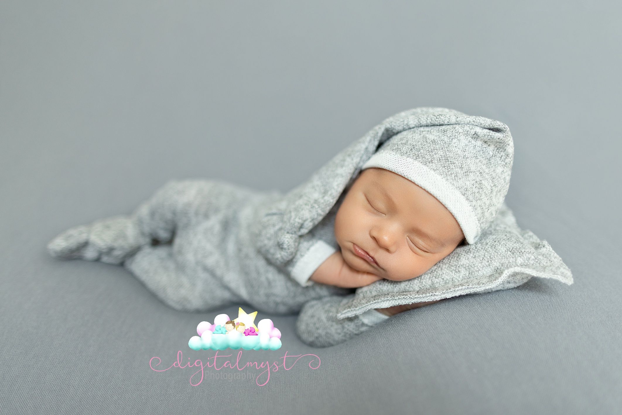 Newborn baby sleeping peacefully wrapped in soft gray fabric on a gray backdrop.