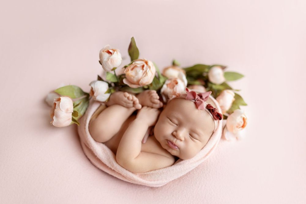 Delicate newborn photography series featuring soft pink tones, floral arrangements, and curled sleeping poses on fabric.