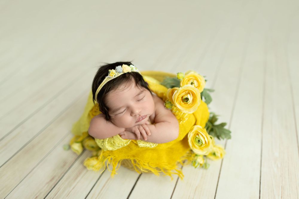 Newborn photography setup with yellow roses and soft fabrics on white wooden background.
