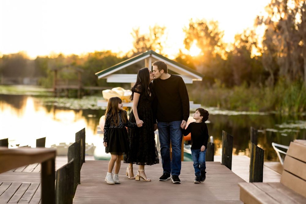 Family photo session at wooden dock during golden hour sunset.