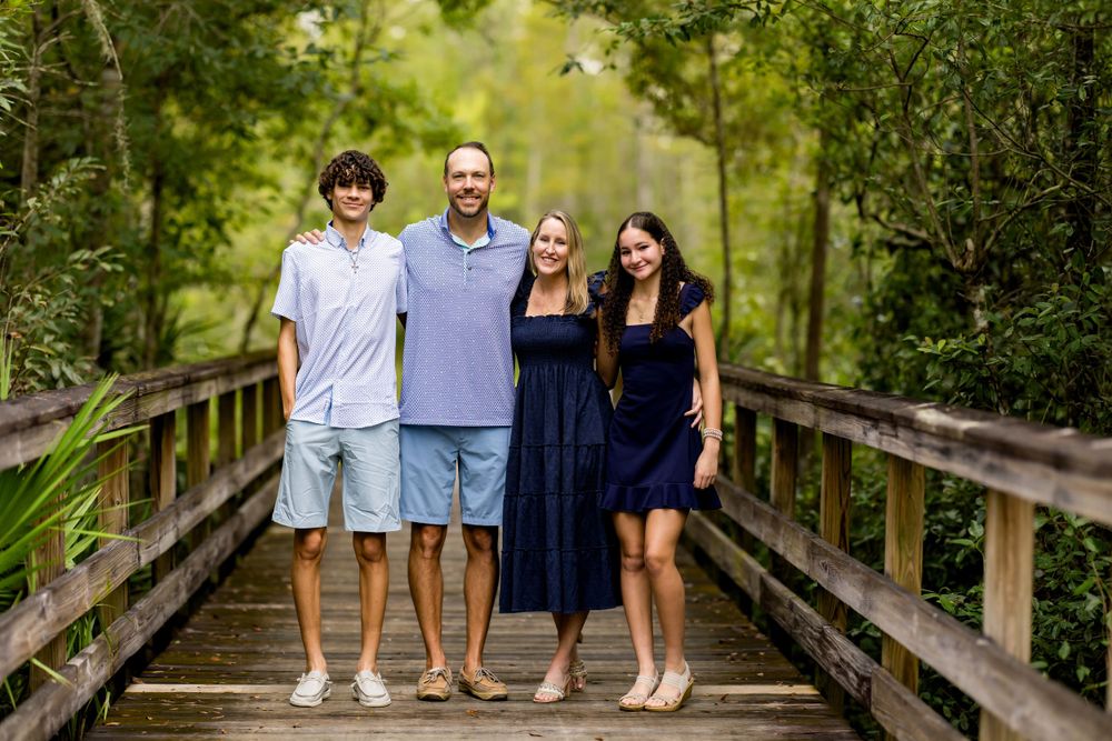 Family portrait on wooden bridge walkway surrounded by lush greenery.