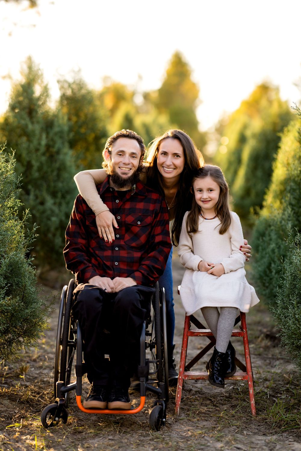 Loving family poses together outdoors among evergreen trees at golden hour.