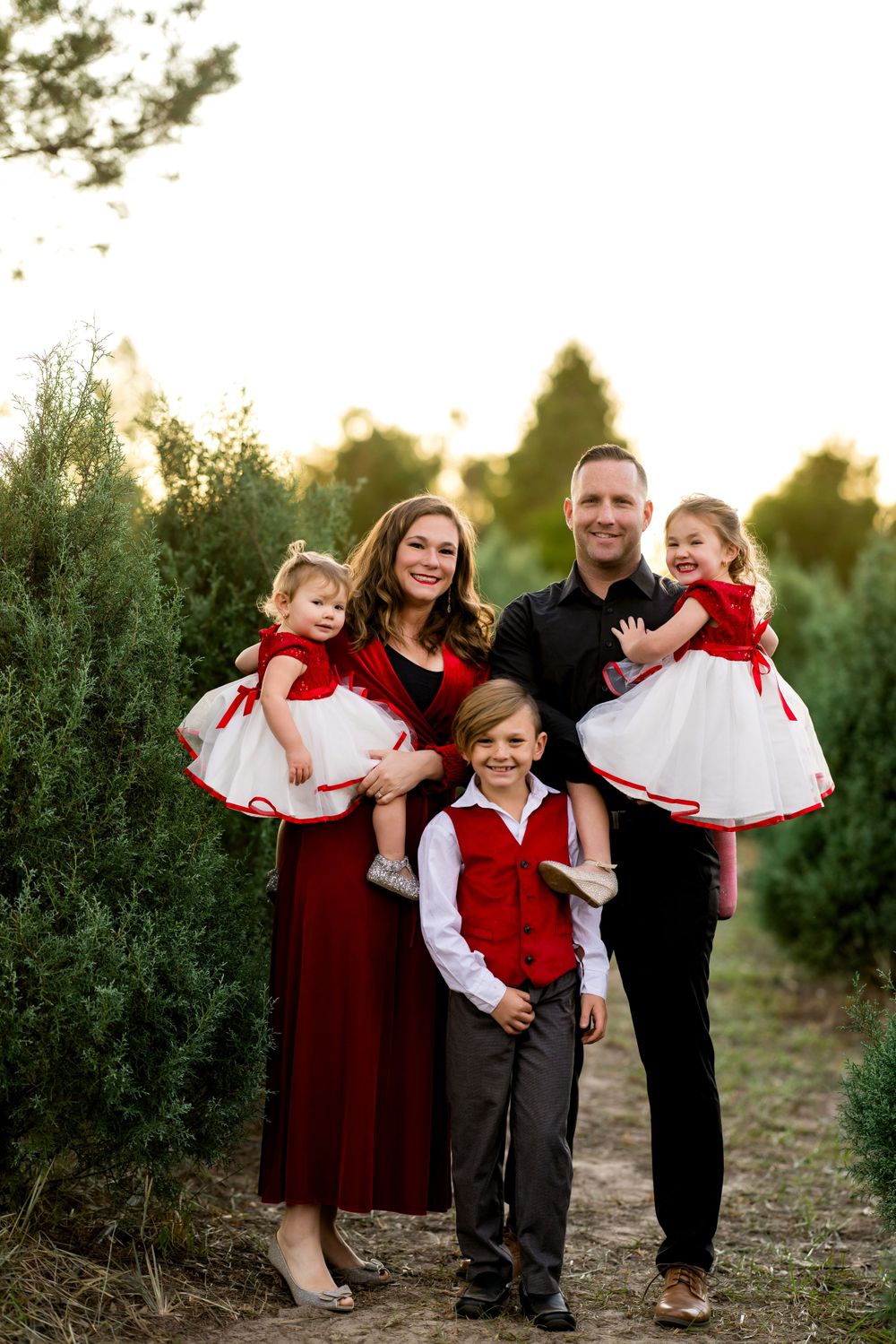 Parents and children gather for holiday photos wearing festive red and white attire among evergreen trees.