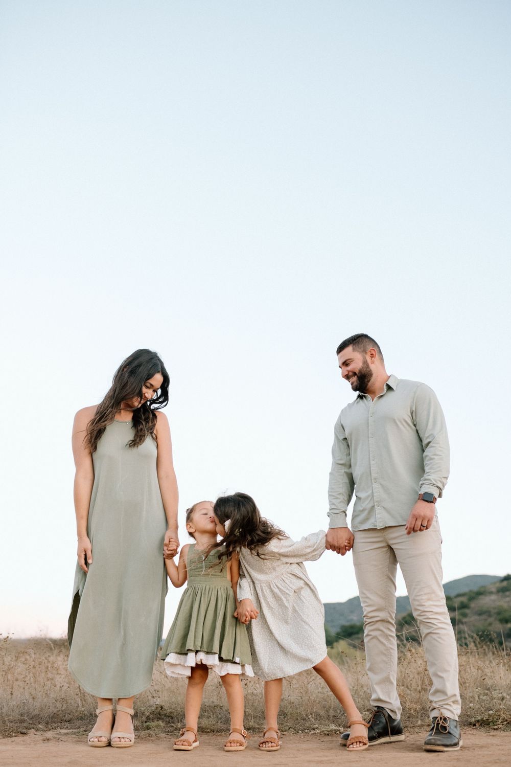 Family in coordinated neutral outfits walking together on a dirt path during family photoshoot in San Diego.