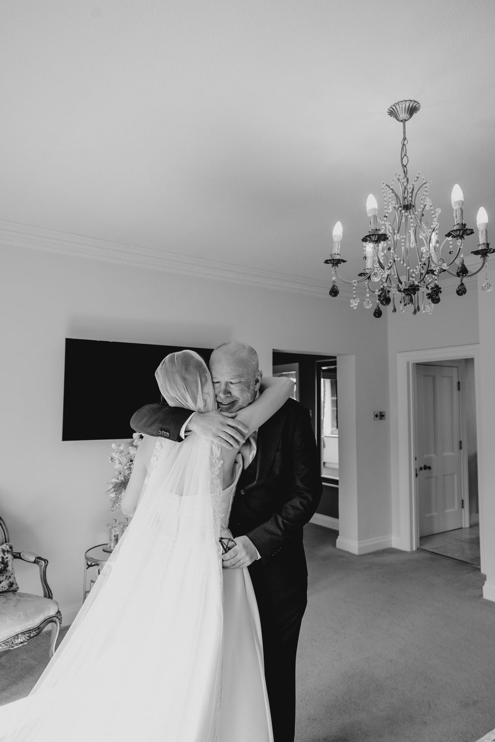 Emotional black and white photo of bride sharing tender hug with father before wedding ceremony.