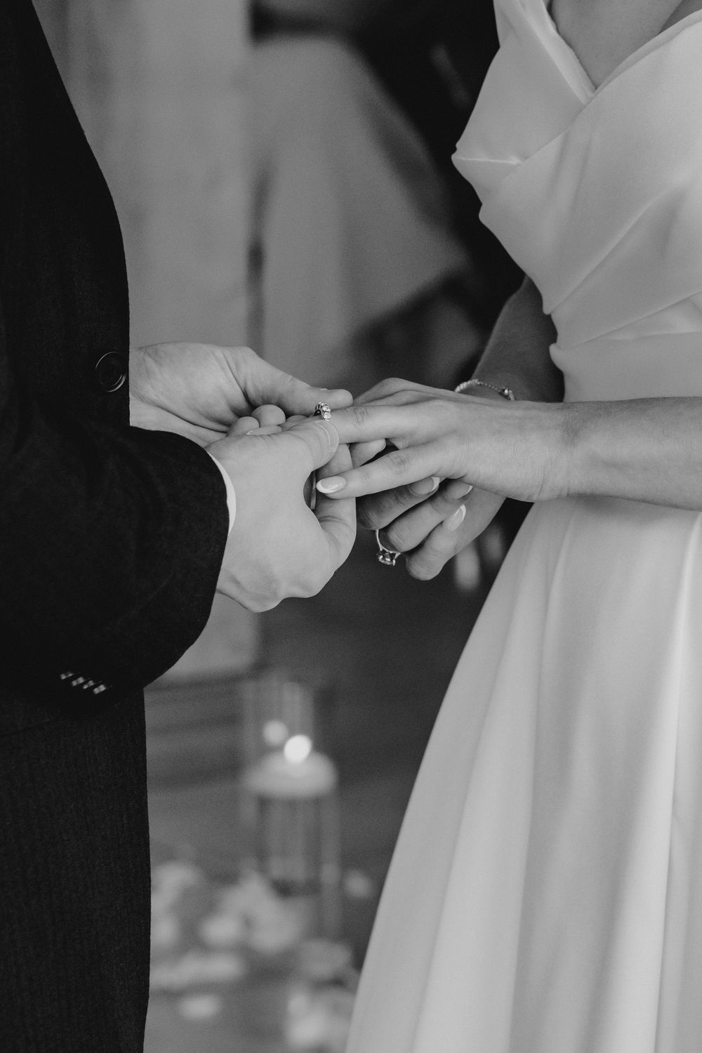 Black and white close-up of groom placing wedding ring on brides finger during ceremony.