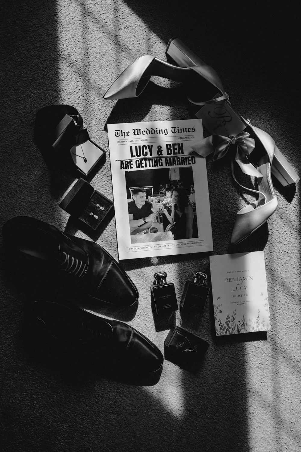 Black and white flat lay of wedding shoes, perfume, and The Wedding Times newspaper announcing Lucy and Ben are getting married.