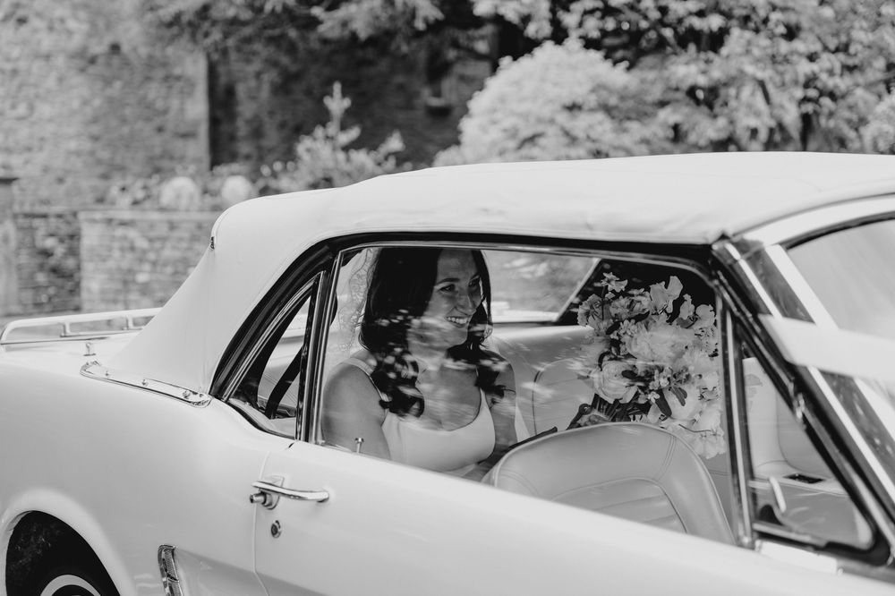 Bride sitting in a classic white convertible car on her wedding day, black and white photography.