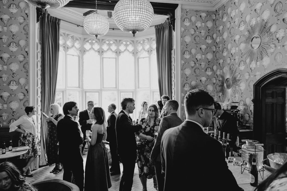 Black and white photo of elegantly dressed guests mingling in an ornate room during a wedding reception.