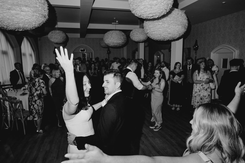 Bride and groom dancing joyfully with guests at lively black and white wedding reception.