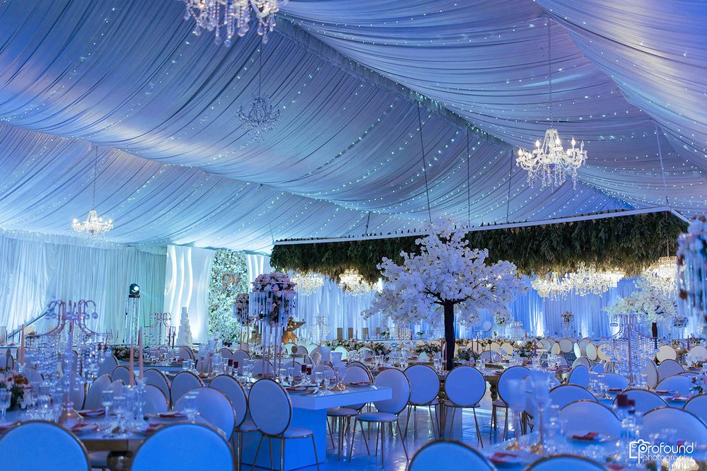 Elegant wedding reception venue with blue lighting, draped ceiling, and crystal chandeliers.