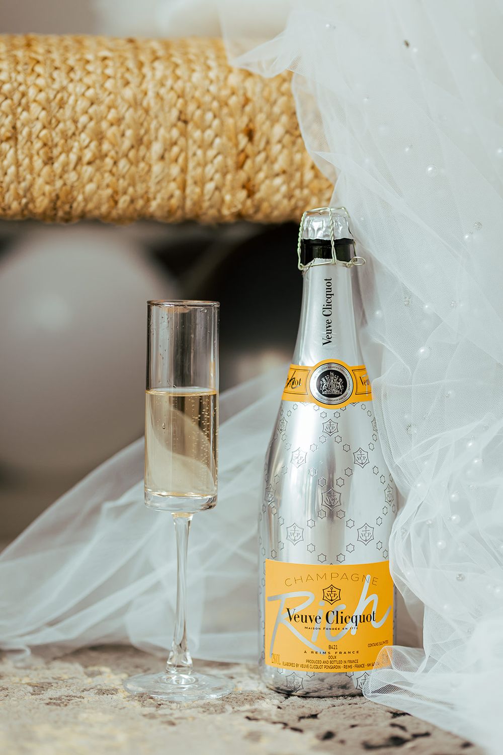A bottle of Veuve Clicquot champagne and glass displayed with elegant white fabric and decor.
