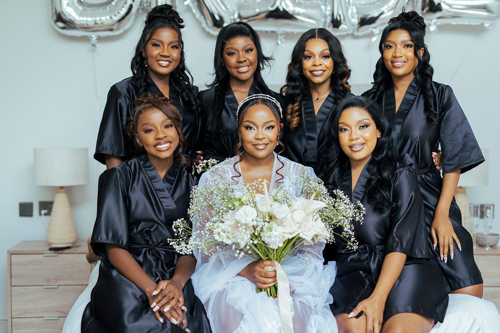 A bridal party in matching black robes poses together with the bride in white.