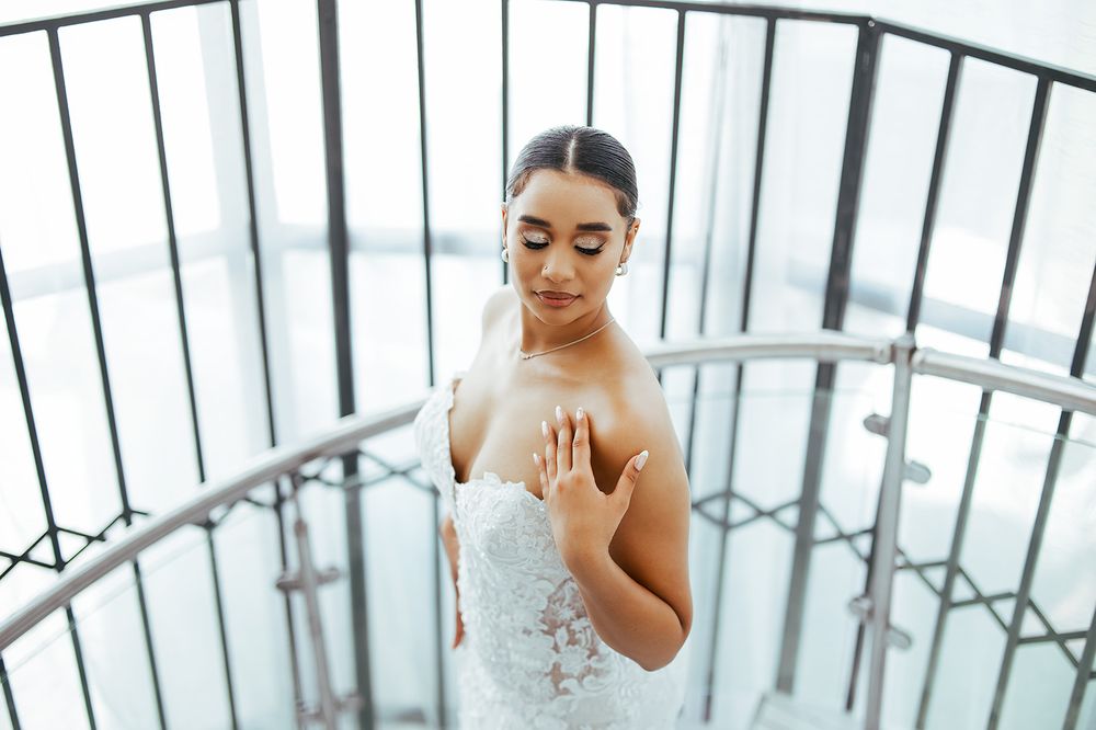 Bride in an elegant lace wedding dress poses thoughtfully on a spiral staircase.