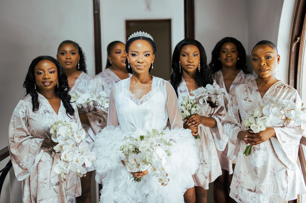 Wedding party in matching white robes holds bouquets during pre-ceremony preparations.