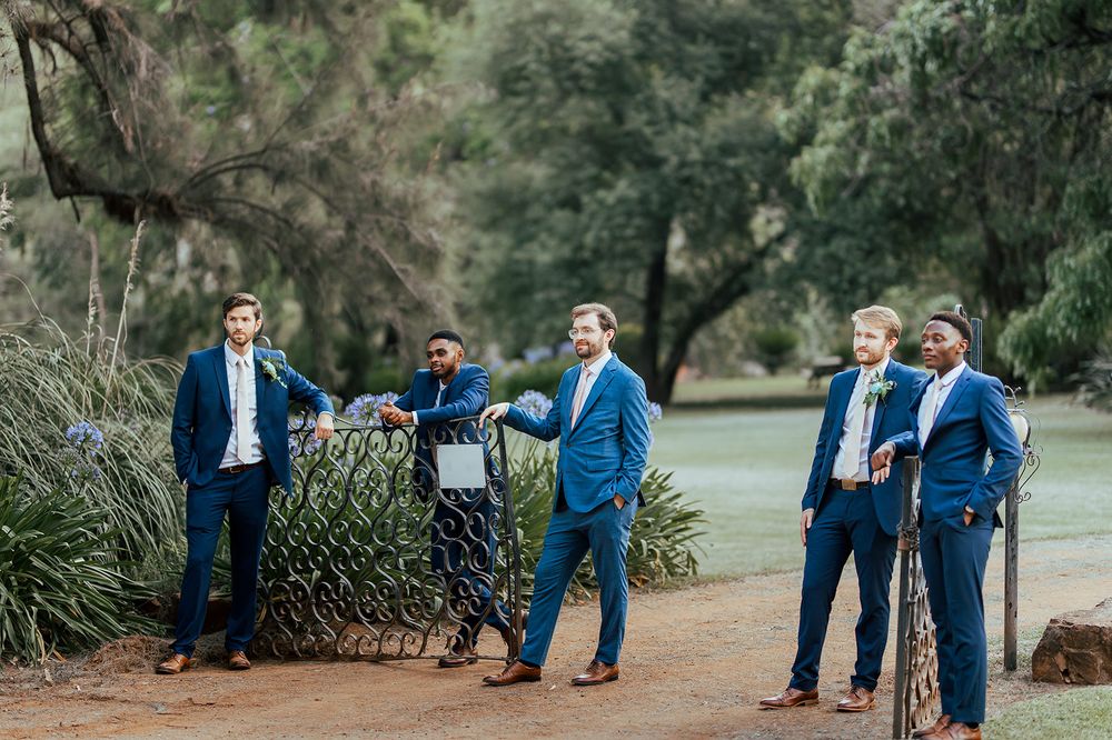 Groomsmen in navy suits gather for casual photo on garden path.