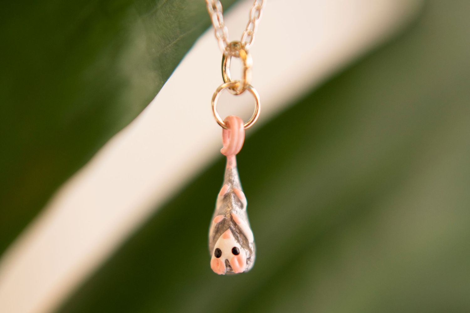 A delicate gold pendant necklace with a pink stone charm shown in soft focus against a blurred green background.